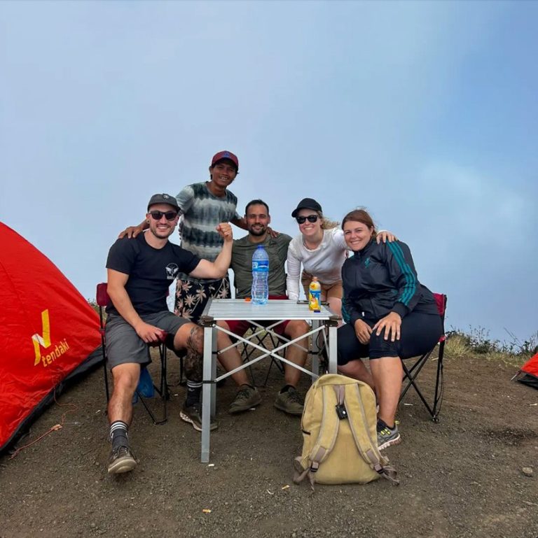 Four hikers and their guide seated at a table outside a tent within their campsite on the way to the Mt. Rinjani Summit