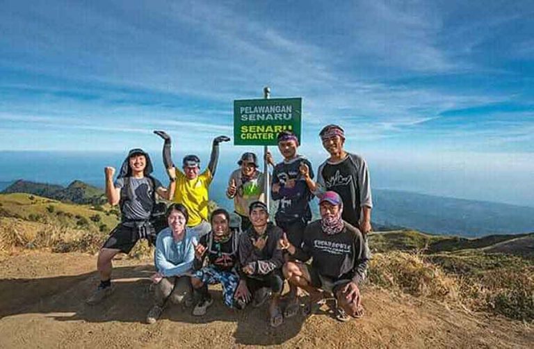 A group of hikers pause with a signpost indicating the Senaru Crater Rim.